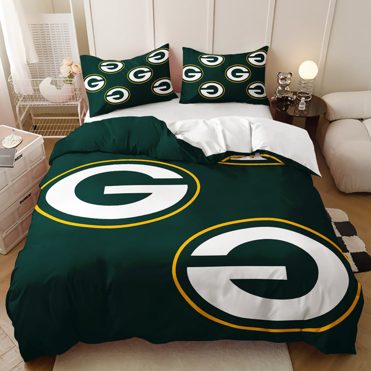 A bed dressed in a Green Bay Packers-themed bedding set, featuring a dark green duvet cover and matching pillowcases with large white and yellow circular 'G' logos